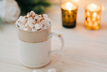 Christmas mug with hot chocolate and marshmallow with cozy garland lights and christmas tree branches on the background