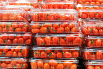 Stacks of red cherry tomatoes in plastic containers close-up in a supermarket.