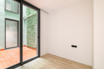 Refurbished white room with big window leading to patio with green walls and vertical gardening. Modern building design.