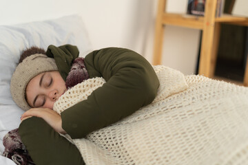 Young woman sleeping in warm clothes covered with blanket. Cold winter. No heating at home. No heating