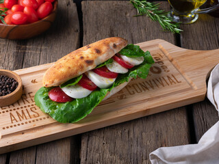 Italian Caprese sandwich with tomato, mozzarella and arugula on wooden cutting board. Panozzo