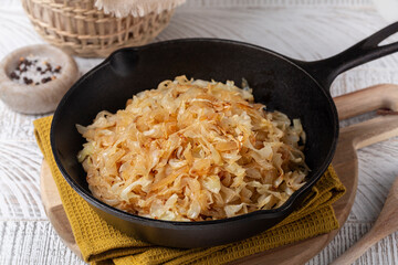 Pan fried Sauerkraut or Crauti. Finely cut white cabbage cooked with fried onion and white wine. White wooden table.