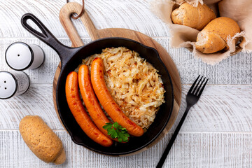 Austrian dinner directly above. Wurstel wiener, sausage or frankfurter and fried crauti or sauerkraut in a cast iron pan. Bread buns.