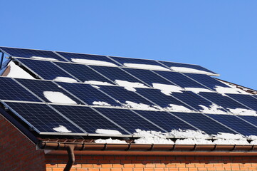 Solar panels covered with snow, on the roof of the cottage. Green energy for heating in winter