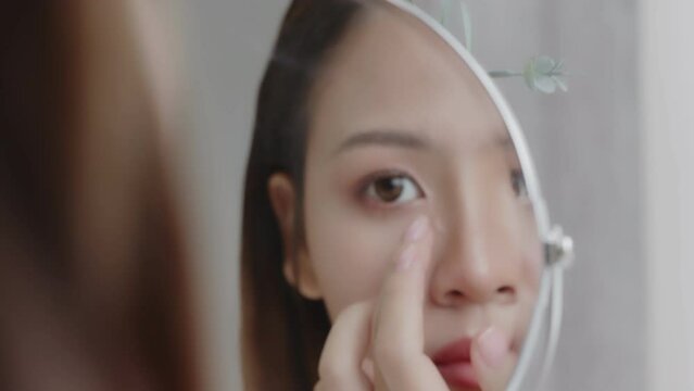 Close up reflection of young Asian woman applying concealer on face.