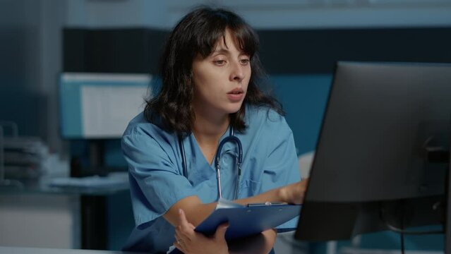 Physician nurse checking illness report on computer while working at patient treatment to help cure disease during night shift in hospital office. Medical assistant looking at papers with expertise