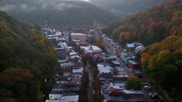 Cinematic shot of small American town in mountains at sunrise. Autumn fall foliage and fog at daybreak. Lights in valley homes as car drives in quiet morning. Rising aerial reveal.