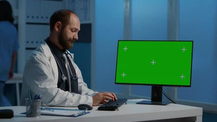 General practitioner typing medical expertise on computer with greenscreen chroma key template working over hours in hospital office. Doctor checking patient report while planning healthcare treatment
