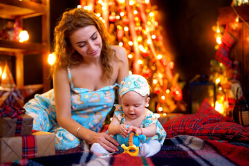 Fototapeta na wymiar Mother playing with baby daughter while sitting near Christmas tree in decorated living room 