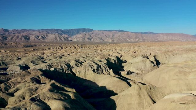 Aerial Landscape Drone Flying Over Hilly Arroyo Tapiado Mud Caves Towards Mountains on Hot, Dry, Sunny Day with Blue Skies