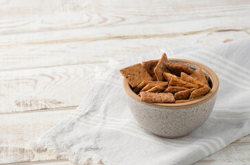 Bowl of dry crackers with tomato and basil on light wood background with napkin