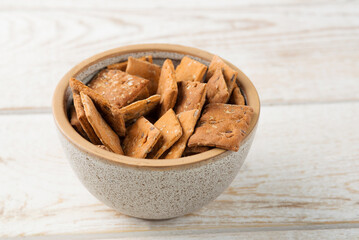 Bowl of dry crackers with tomato and basil taste on light wood background. close-up