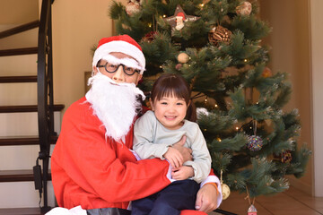 Fototapeta na wymiar クリスマスツリーの前でサンタクロースに抱っこされて笑う女の子