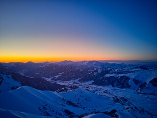 Fototapeta na wymiar Vertical aerial panorama of snowy mountain ridge on winter sunrise. Stunning mountains range covered with snow at sunset afterglow. Caucasus mountain peaks skyline in the twilight golden hour.
