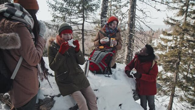 Group of stylish young Black and Caucasian friends spending weekend together hiking in mountains on winter day having lunch break