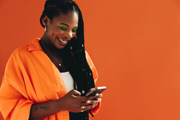Fototapeta Smiling black woman sending a text message on her smartphone in a studio obraz