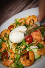 Recipe for rocket salad, endive, tomato, cucumber, soft-boiled egg, fried shrimp with paprika, smoked salmon and nuts. High quality photo