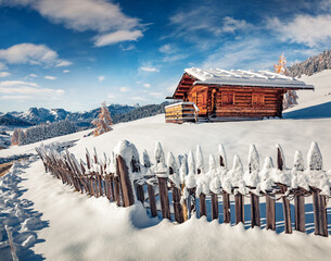 Snowy winter scene of Dolomite Alps. Wooden chalet on the hill of Alpe di Siusi village. Bright...