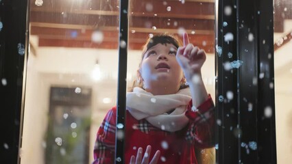 Adorable child look through the window and admiring first snow flakes.