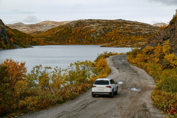 Fototapeta premium A white car drives along a beautiful dirt road along northern landscapes
