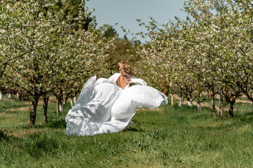 A woman in a white dress runs through a blossoming cherry orchard. The long dress flies to the sides, the bride runs rejoicing in life.