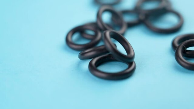 Sealing rubber rings falling on a blue colored background in slow motion. Industrial hydraulic spare parts. Rotation. Macro