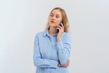 Upset and unhappy blonde woman talking on mobile phone, conversation on smartphone, standing over white background in casual blue shirt. Cellphone, cellular concept