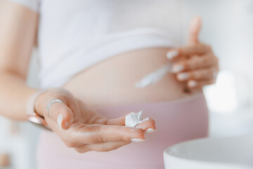 Closeup cream in hand of pregnant woman for belly to moisturize skin and improve elasticity to prevent stretch marks. Concept care health pregnancy