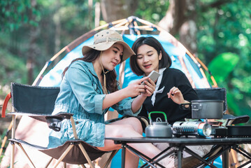 Asian pretty woman and girlfriend use smartphone selfie on camping.