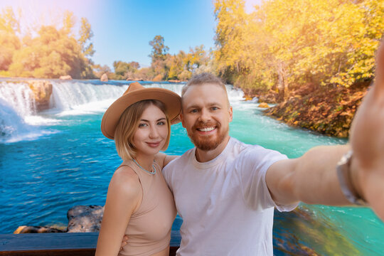 Happy tourist couple man and woman in hat holds action camera and takes picture of selfie background waterfall Manavgat Antalya, Turkey
