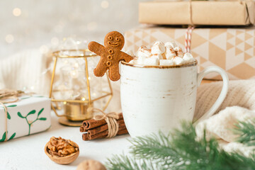 Obraz na płótnie Canvas Gingerbread man cookie in cup of hot cocoa or coffee with marshmallow, fir tree, gifts and warm cozy sweater. Christmas greeting card, lights background. Xmas holiday decorations with copy space.