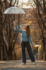 Beautiful girl with transparent umbrella. Happy young woman with long hair walks in autumn park.