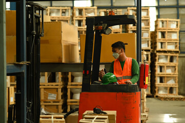 Fototapeta na wymiar Male warehouse worker moving cardboard boxes of goods with forklift between rows of tall shelves