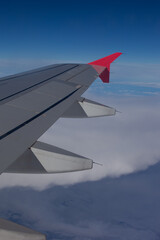 Fototapeta premium View of an airplane wing in flight. The wing of a medium-haul aircraft above the clouds and with the blue sky. The atmosphere of a journey.