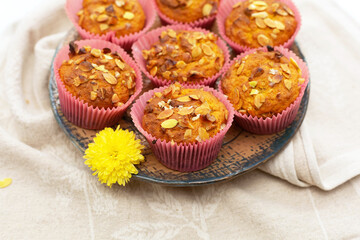 Homemade pumpkin cupcakes and small yellow flower lie in round ceramic plate on linen napkin.Autumn baking for Thanksgiving and Halloween. Selective focus. Close-up.
