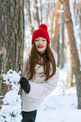 Dreaming girl with closed eyes stands in a snowy park. Portrait of young girl in red hat with bubo in winter forest. Vertical frame