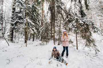 A happy boy is sitting in the snow next to a girl in the forest
