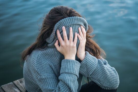 The woman hid her face in a sweater, sitting by the sea.