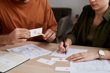 Male tutor of Chinese language pointing at paper card with hieroglyph while sitting in front of...