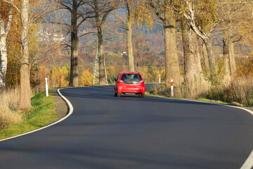 Kręta droga asfaltowa biegnie między drzewami jesienią. 
