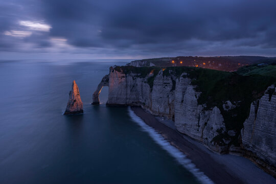 France, Normandy, Etretat, Falaise dAval cliffs and Aiguille dEtretat sea stack at cloudy dusk