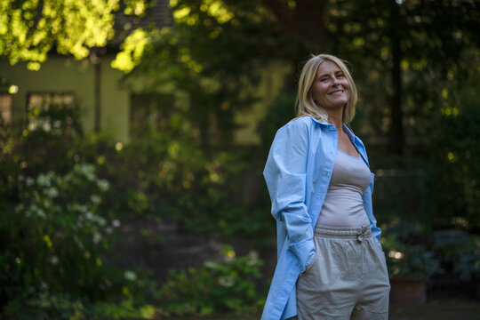 Happy mature woman standing with hands in pockets at garden