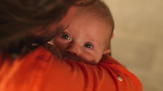 Close-up portrait of cute Caucasian baby sitting in arms of father. Little girl looking directly at camera. Back shot of daddy kissing forehead of child