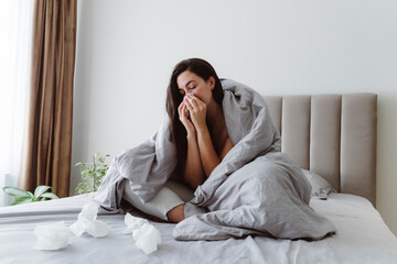 Ill woman blowing nose in tissue on bed at home