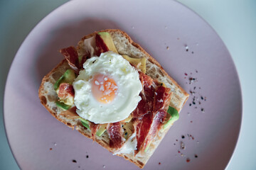 Close up view of avocado toast with ham and egg served on a plate.