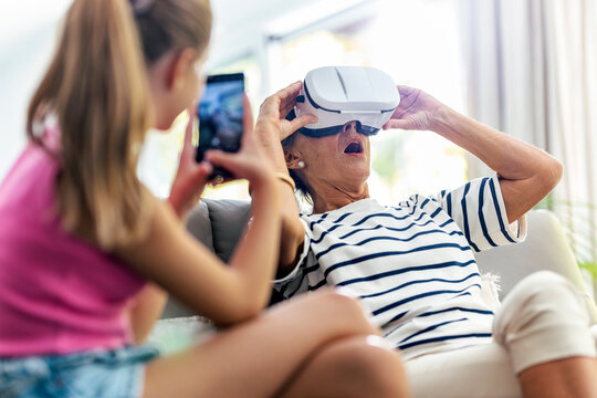 Girl photographing grandmother wearing virtual reality headset at home