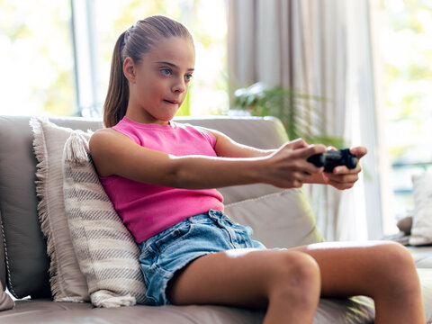 Determined girl playing video game with joystick sitting on sofa at home