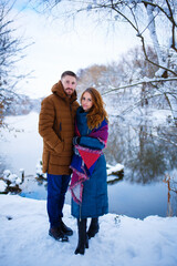 Fototapeta na wymiar A young couple walks in a snowy park in winter and warms up with tea. The beauty of nature before the New Year. Copy space
