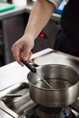 Chef hand using thermometer on boiling water vertical stills.