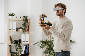 Engineer watching robotic arm through VR goggles in office